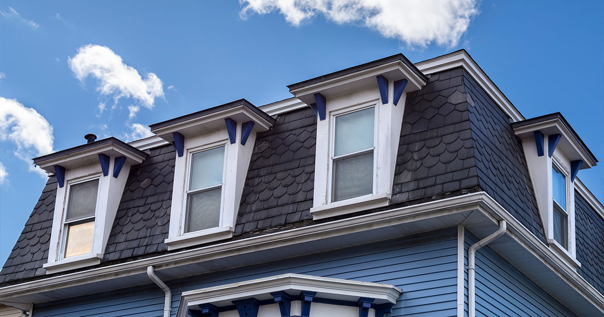 Close-up of a blue historic house roof with dormer windows under a bright blue sky with clouds.