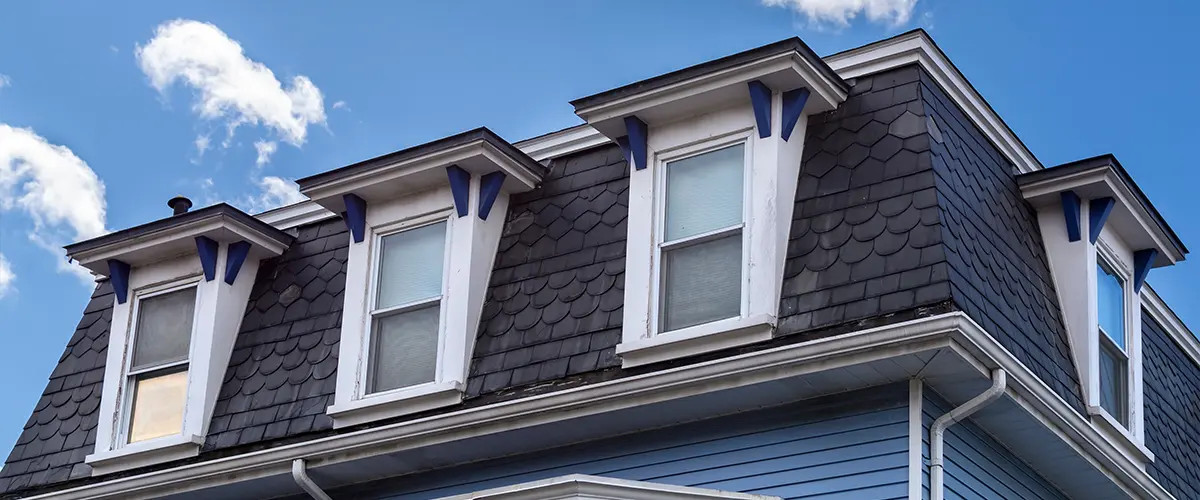 Close-up of a blue historic house roof with dormer windows under a bright blue sky with clouds.