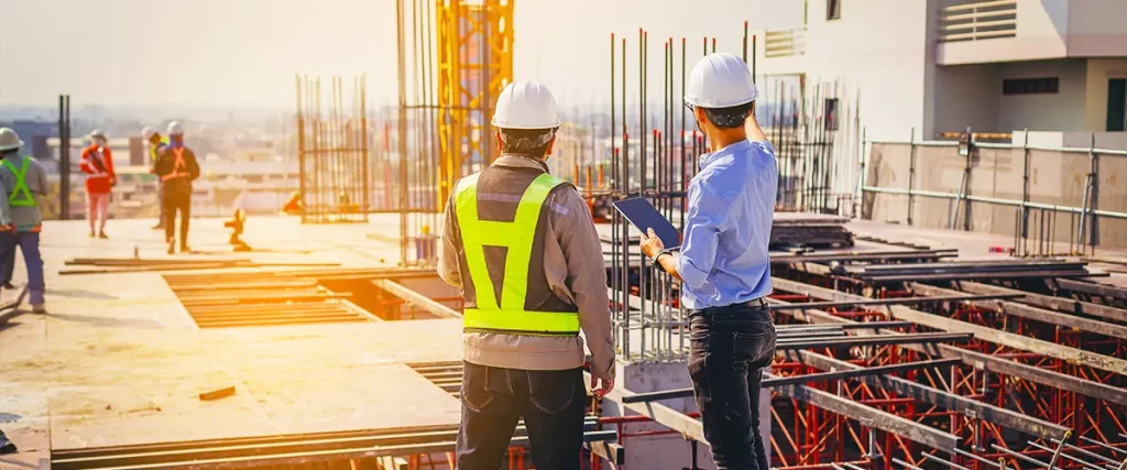 Construction workers in safety gear discussing progress at a building site during sunset