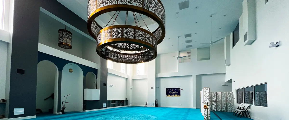 Elegant mosque interior with vibrant turquoise carpet, intricate chandeliers, and high ceilings, showcasing modern Islamic architecture.