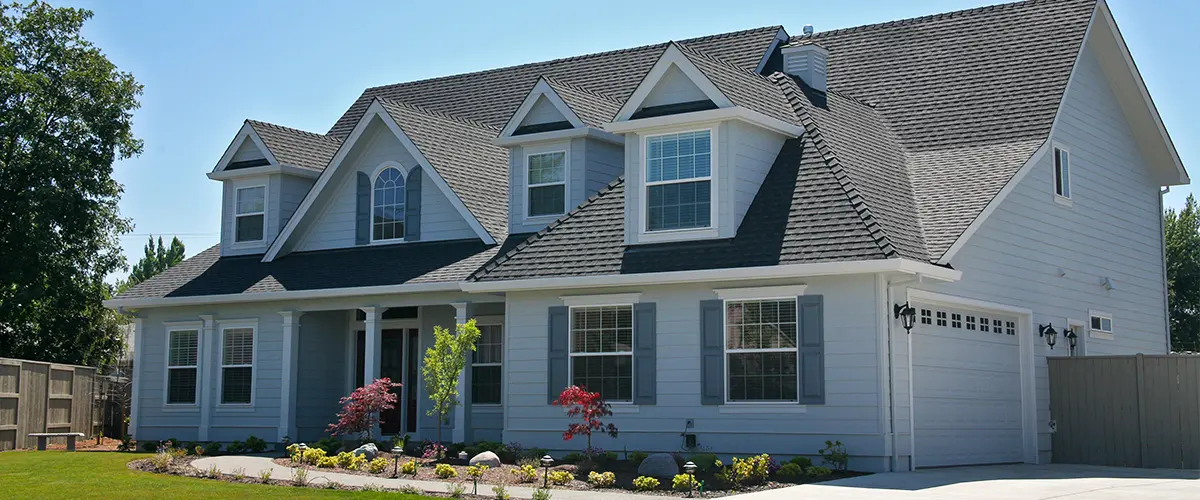 Large, modern two-story home with gray siding, black shingle roof, and well-maintained front lawn landscaping.