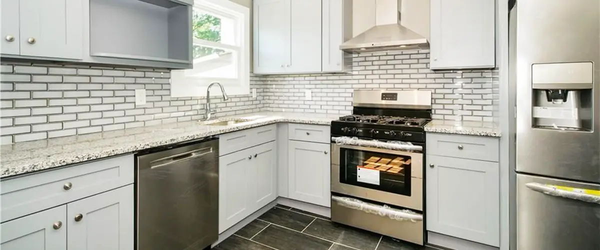 Modern kitchen renovation with light gray cabinets, stainless steel appliances, granite countertops, and subway tile backsplash.