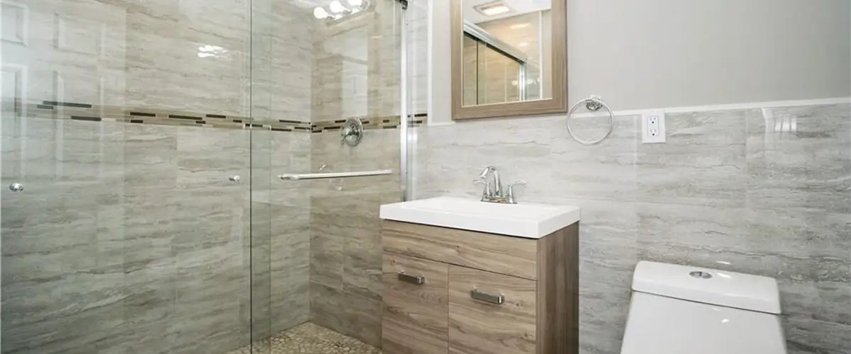 Renovated bathroom with glass shower enclosure, wood vanity, modern fixtures, and elegant gray tile walls for a clean finish.