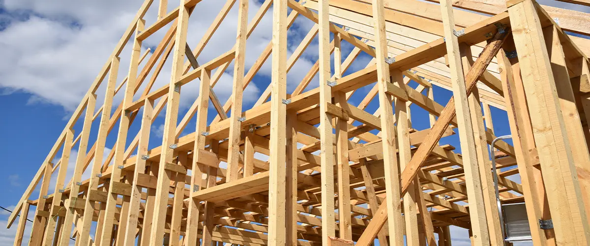 Wooden house frame under construction against a cloudy blue sky.