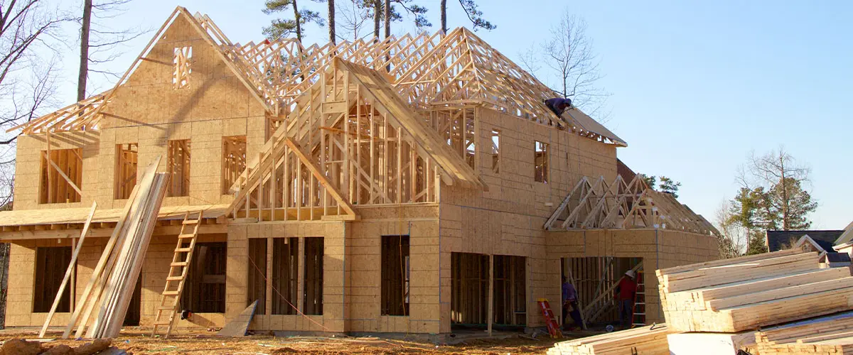 Wooden two-story house under construction with workers and building materials on-site.