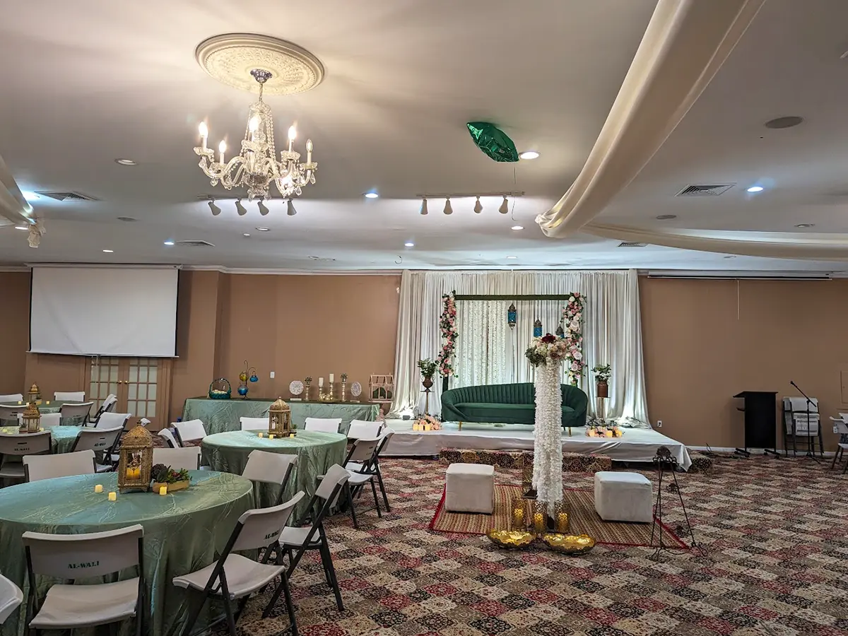 Elegant event hall setup with chandeliers, green tablecloths, and a decorative stage centerpiece for celebrations.