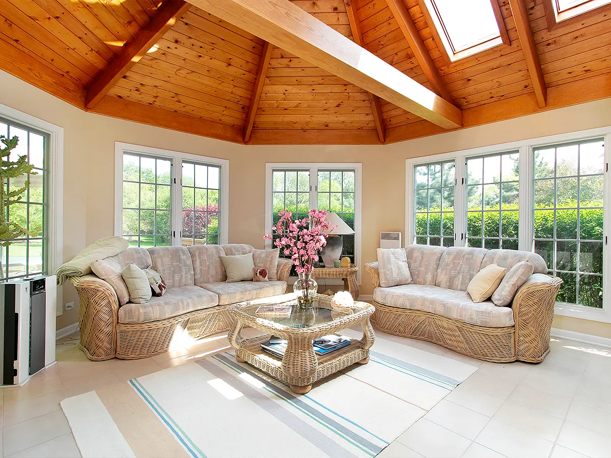 Spacious sunroom featuring wicker furniture, vaulted wooden ceiling, and panoramic views of the garden.