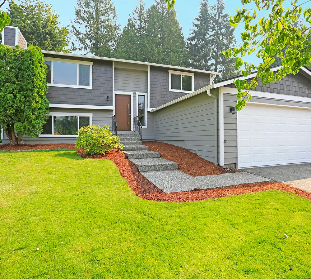 Modern suburban home with a well-landscaped front yard, gray siding, and a white garage door.