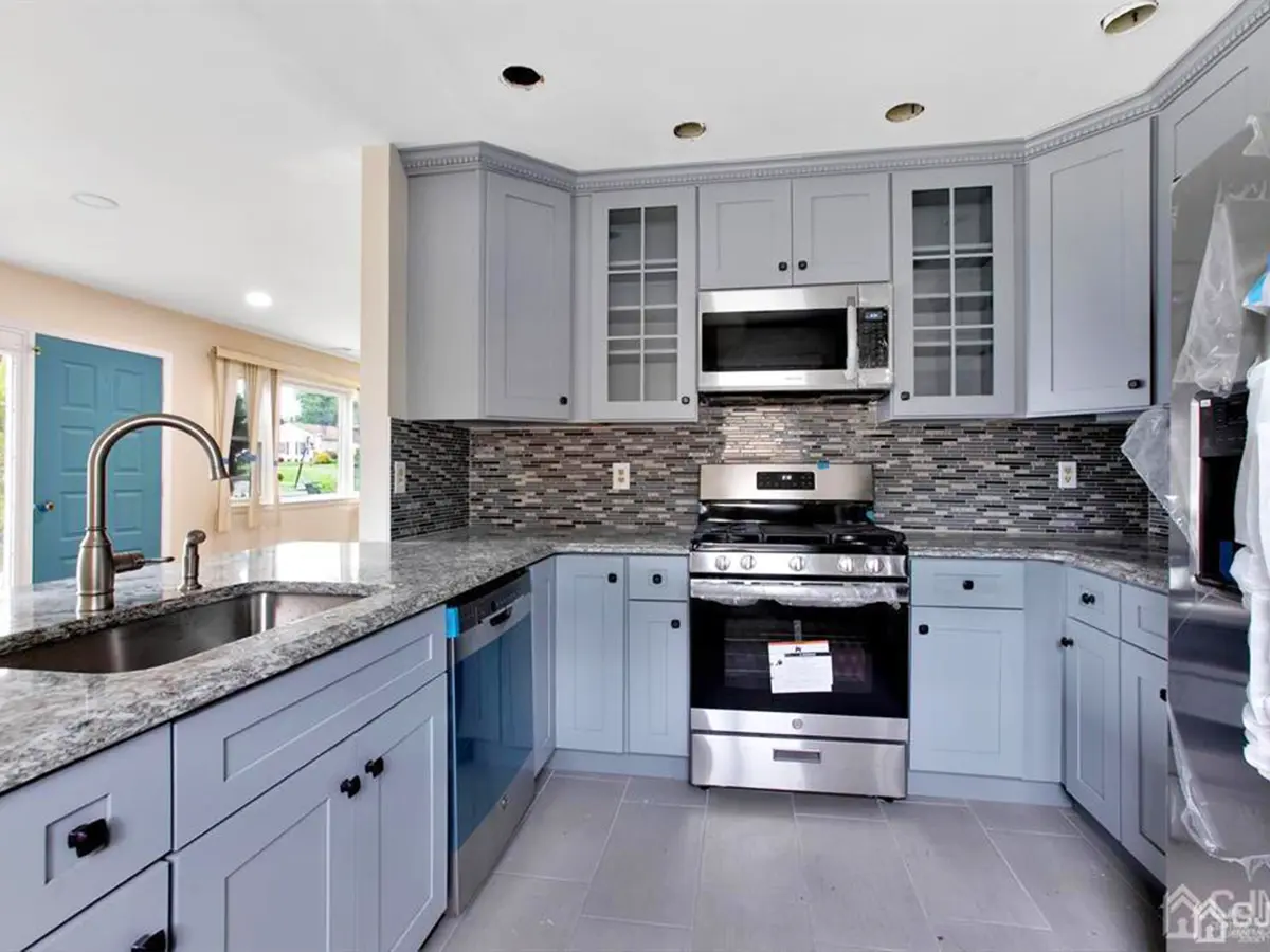 Stylish kitchen with light gray cabinets, mosaic backsplash, and granite countertops in an open layout.