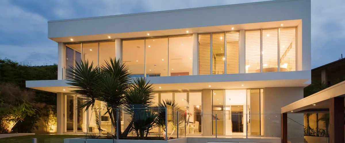 Stunning contemporary home with a glass facade, illuminated interiors, and a sleek architectural design.