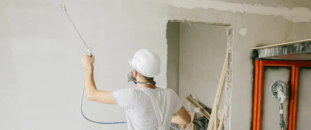 Contractor spraying paint on interior drywall