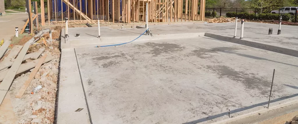 Newly poured and cured concrete slab-on-grade foundation showing pre-installed plumbing lines, a common foundation type for custom homes in areas with clay soil.