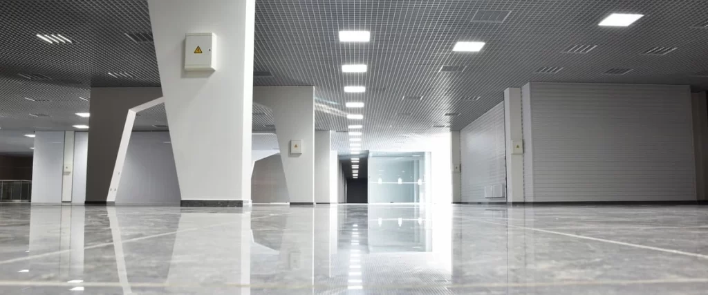 A wide view of a freshly finished empty commercial office space featuring glossy grey tiled floors, white structural columns, and a standard drop ceiling grid.