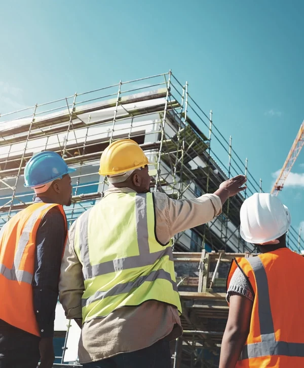 A team of construction managers on a building site pointing towards a structure with scaffolding, overseeing a project in Perth Amboy, NJ.